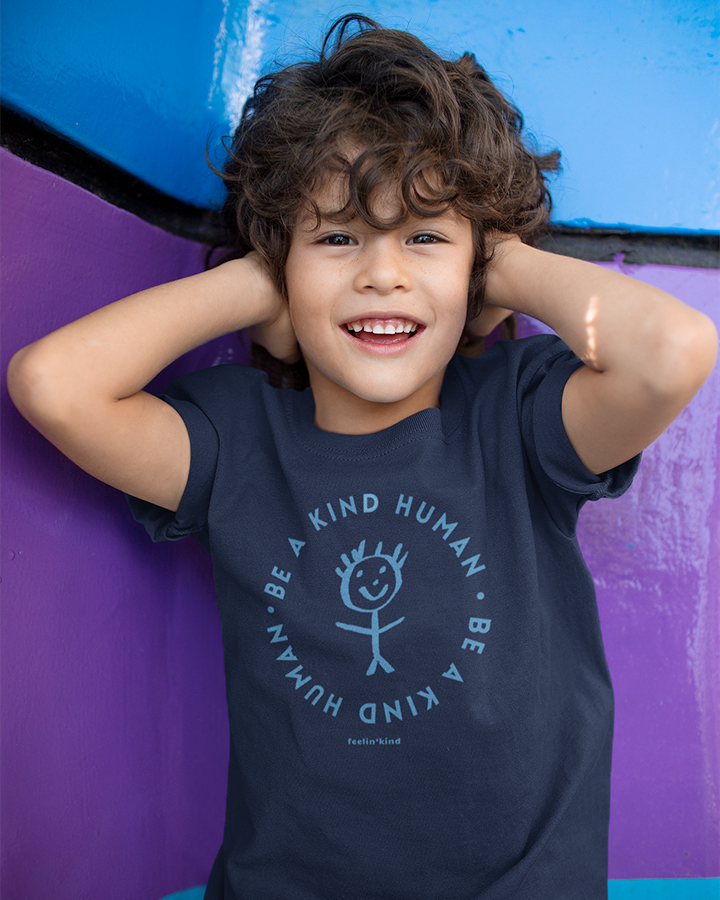 Boy wearing Be a Kind Human kid’s t-shirt featuring a kids drawing of a person in the center.